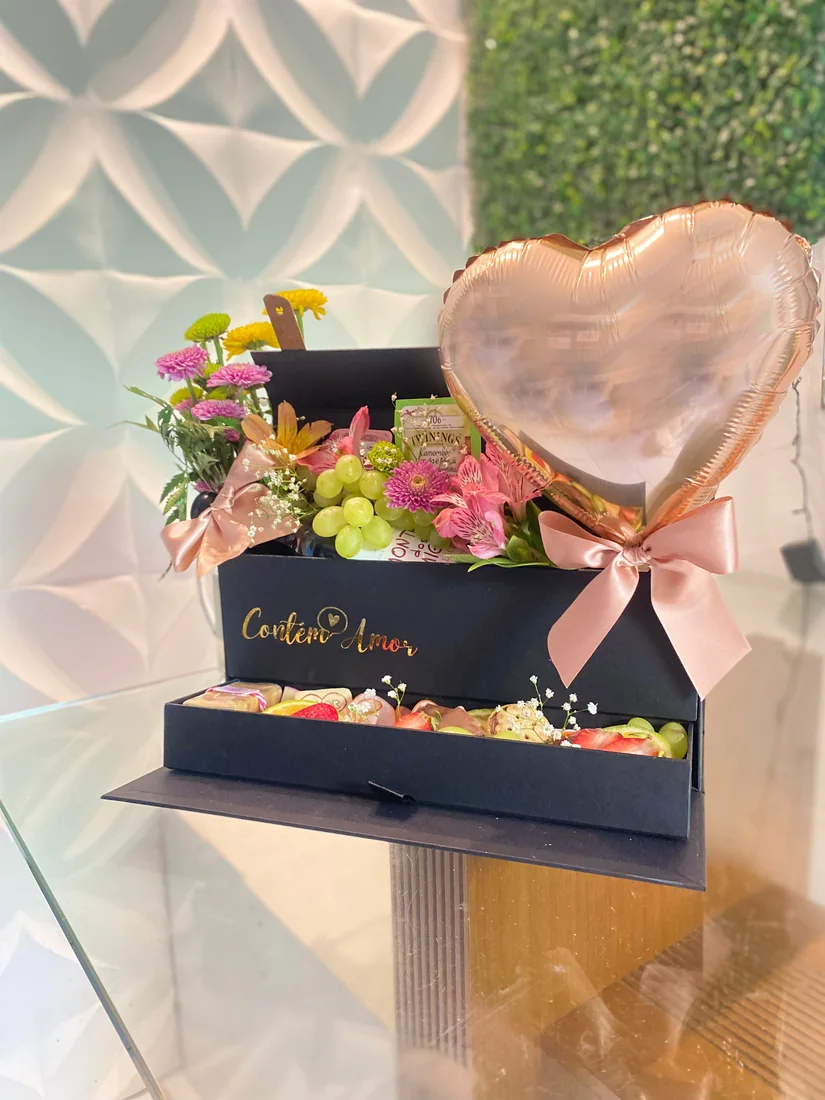Caixa preta com balão de coração, flores, uvas e laço rosa.
