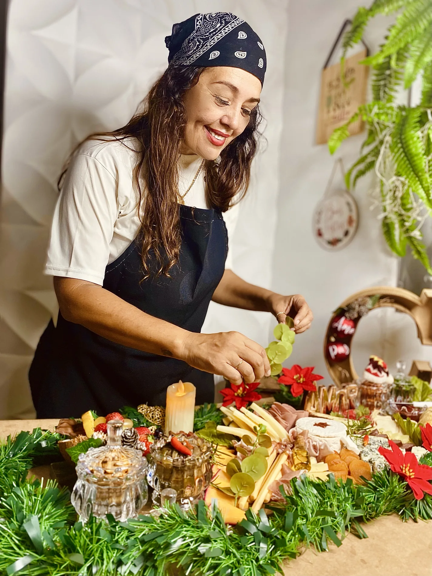 Mesa de grazing food com frios, frutas, flores e itens de celebração.